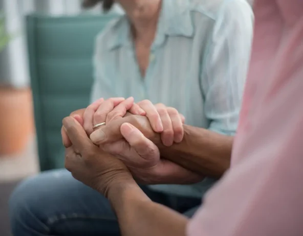 pexels-kampus-8441852 Two people holding hands during a supportive conversation.